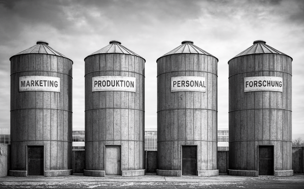 Silodenken: Wenn die größte Konkurrenz die eigenen Kollegen sind 1 Vier Silos beschriftet mit Marketing, Produktion, Personal und Forschung – Symbol für Silodenken in Organisationen neumacher Unternehmensberatung